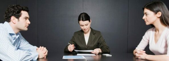 Три человека за столом: мужчина и женщина слева и справа, а посредине женщина в деловом костюме, которая что-то записывает в документы